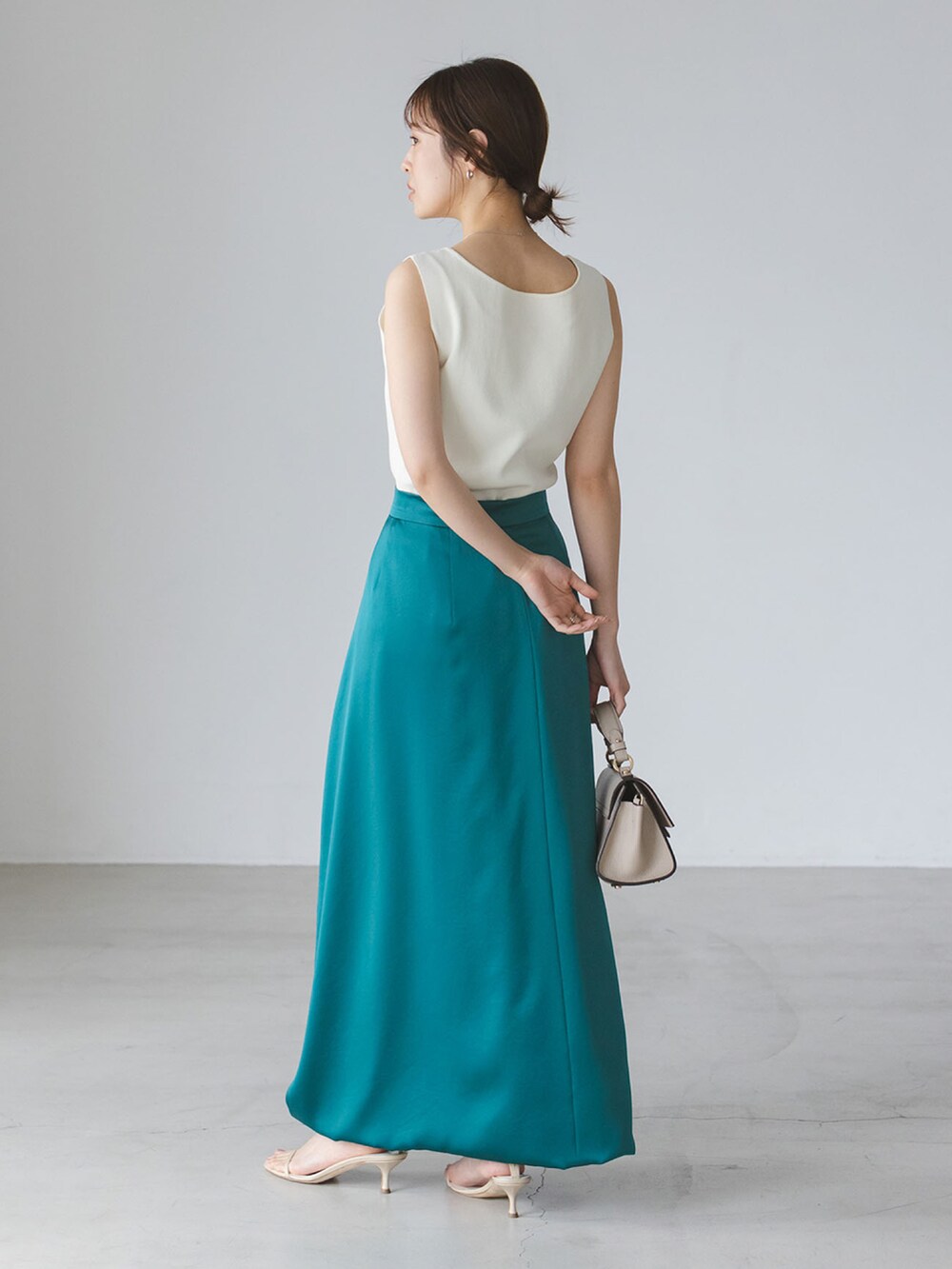 ホワイト系のタンクトップ、グリーン系のスカート、ベージュ系のショルダーバッグを着用したレディースの春コーディネートの2枚目の写真