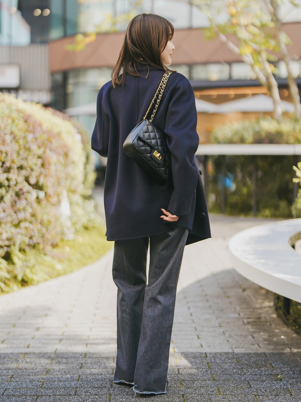ブルー系のチェスターコート、ブラック系のデニムパンツ、ブラック系のブーツを着用したレディースの秋コーディネートの3枚目の写真
