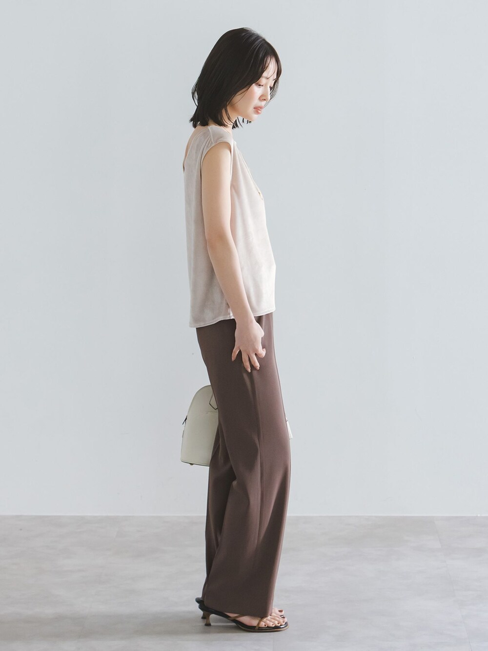 ブラウン系のスラックス、ベージュ系のTシャツ/カットソー、ホワイト系のボストンバッグを着用したレディースの夏コーディネートの2枚目の写真