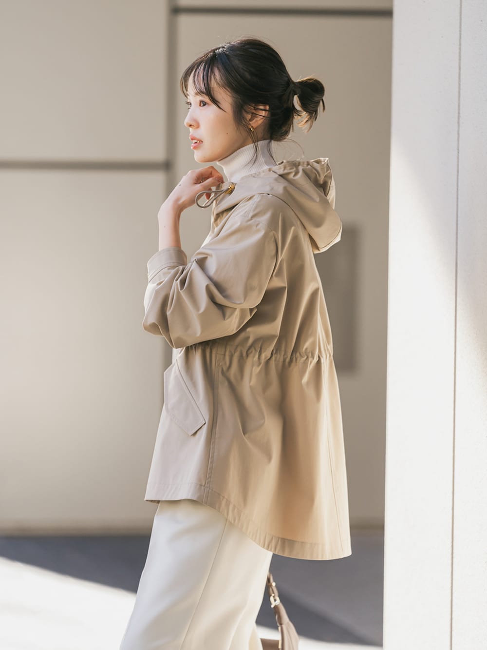 ベージュ系のマウンテンパーカー、ブラウン系のショルダーバッグ、ホワイト系のスラックスを着用したレディースの冬コーディネートの4枚目の写真