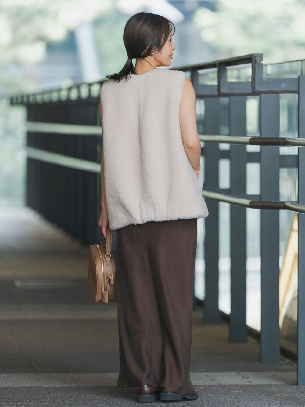 ホワイト系のベスト、ブラウン系のスカート、イエロー系のショルダーバッグを着用したレディースの秋コーディネートの3枚目の写真