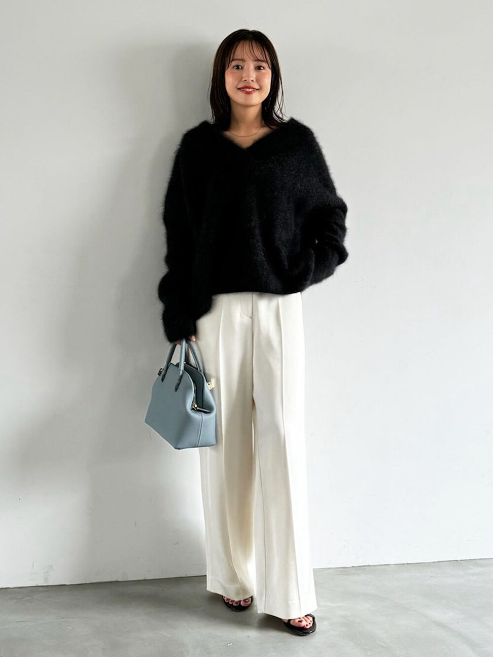 グレー系のニット/セーター、ブルー系のショルダーバッグ、ホワイト系のスラックスを着用したレディースの秋コーディネートの2枚目の写真