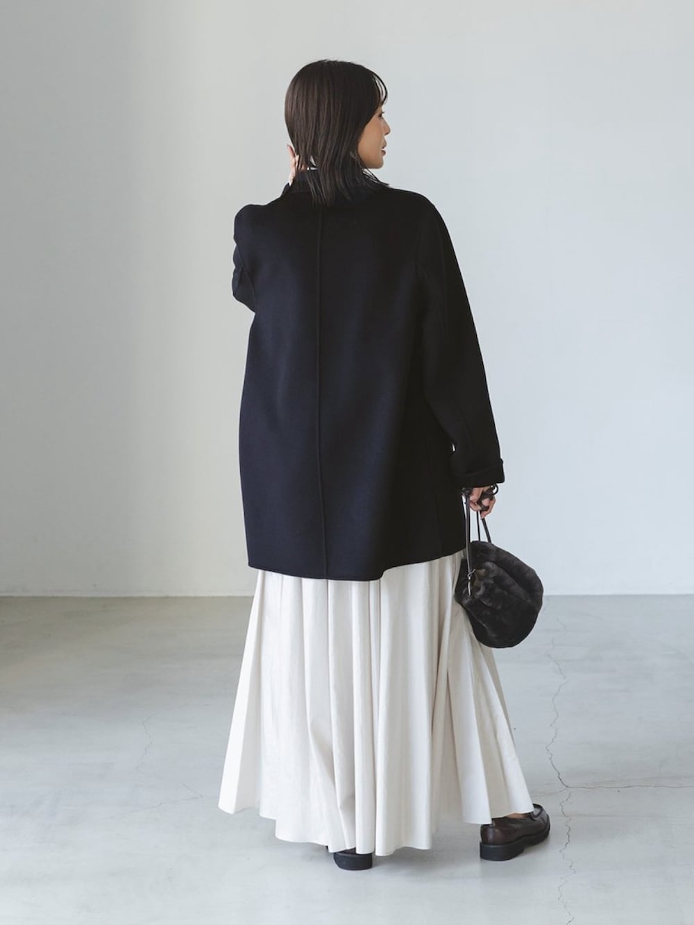 ブルー系のチェスターコート、ベージュ系のスカート、ホワイト系のニット/セーターを着用したレディースの秋コーディネートの2枚目の写真