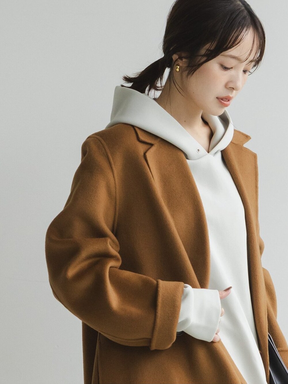 イエロー系のチェスターコート、ホワイト系のスウェット、グレー系のスカートを着用したレディースの秋コーディネートの3枚目の写真