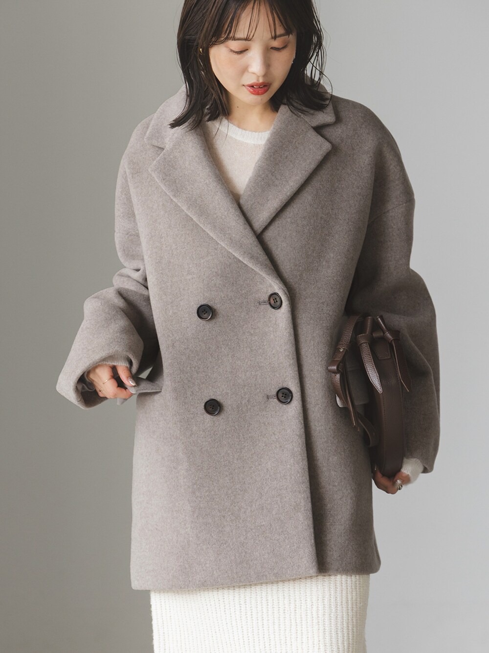 ベージュ系のピーコート、ホワイト系のスカート、ブラウン系のショルダーバッグを着用したレディースの秋コーディネートの3枚目の写真