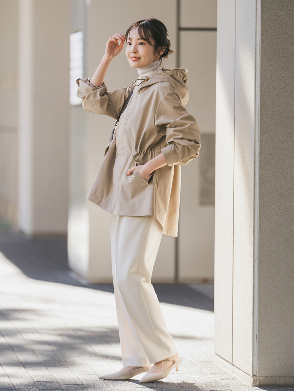 ベージュ系のマウンテンパーカー、ブラウン系のショルダーバッグ、ホワイト系のスラックスを着用したレディースの冬コーディネートの2枚目の写真