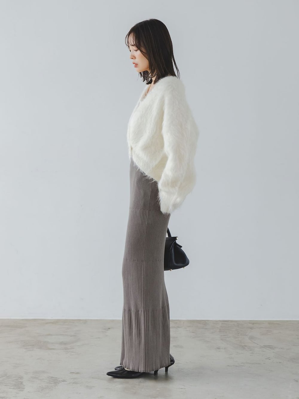 ホワイト系のカーディガン/ボレロ、グレー系のスカート、イエロー系のボストンバッグを着用したレディースの秋コーディネートの2枚目の写真