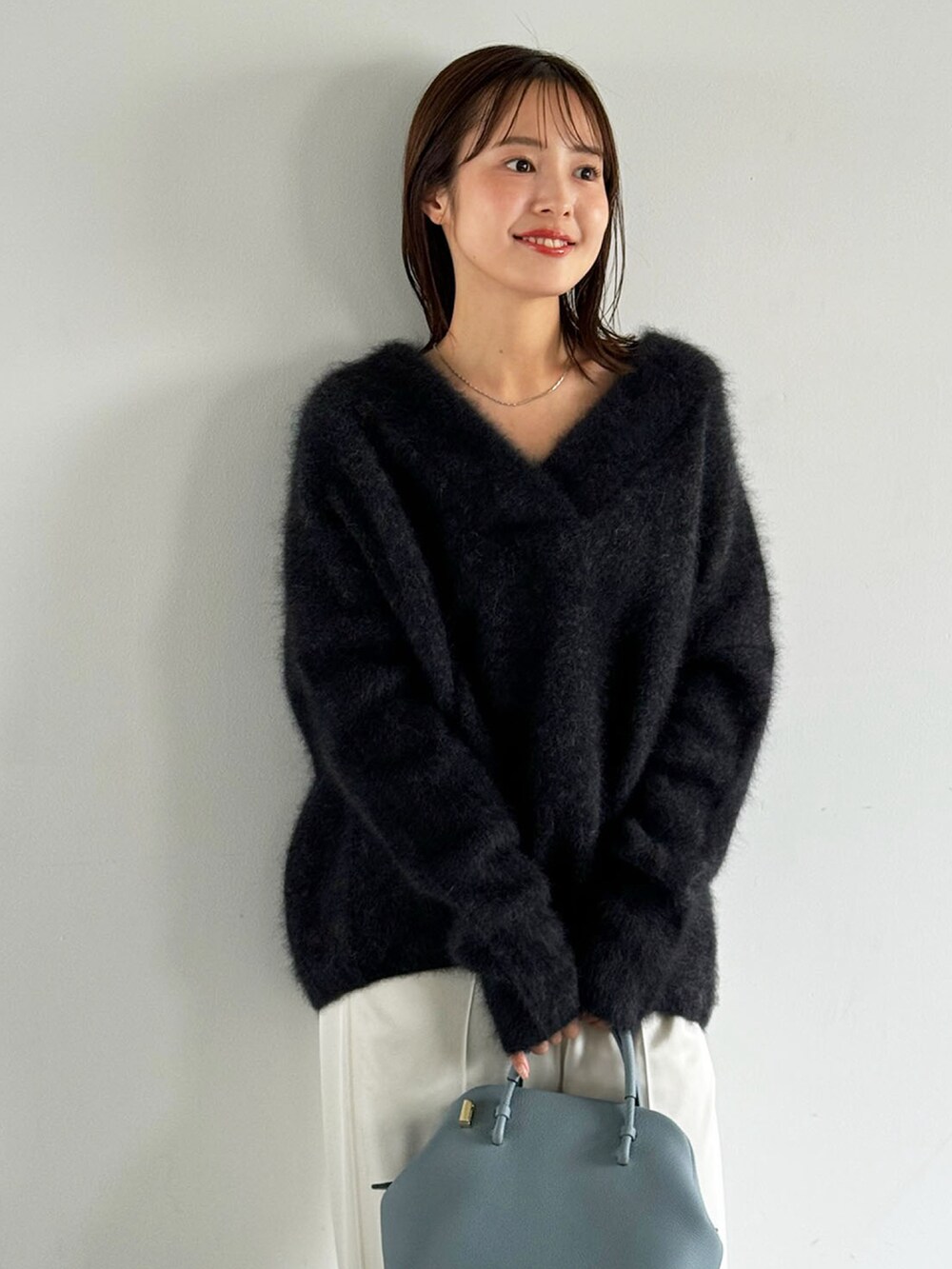 グレー系のニット/セーター、ブルー系のショルダーバッグ、ホワイト系のスラックスを着用したレディースの秋コーディネートの3枚目の写真