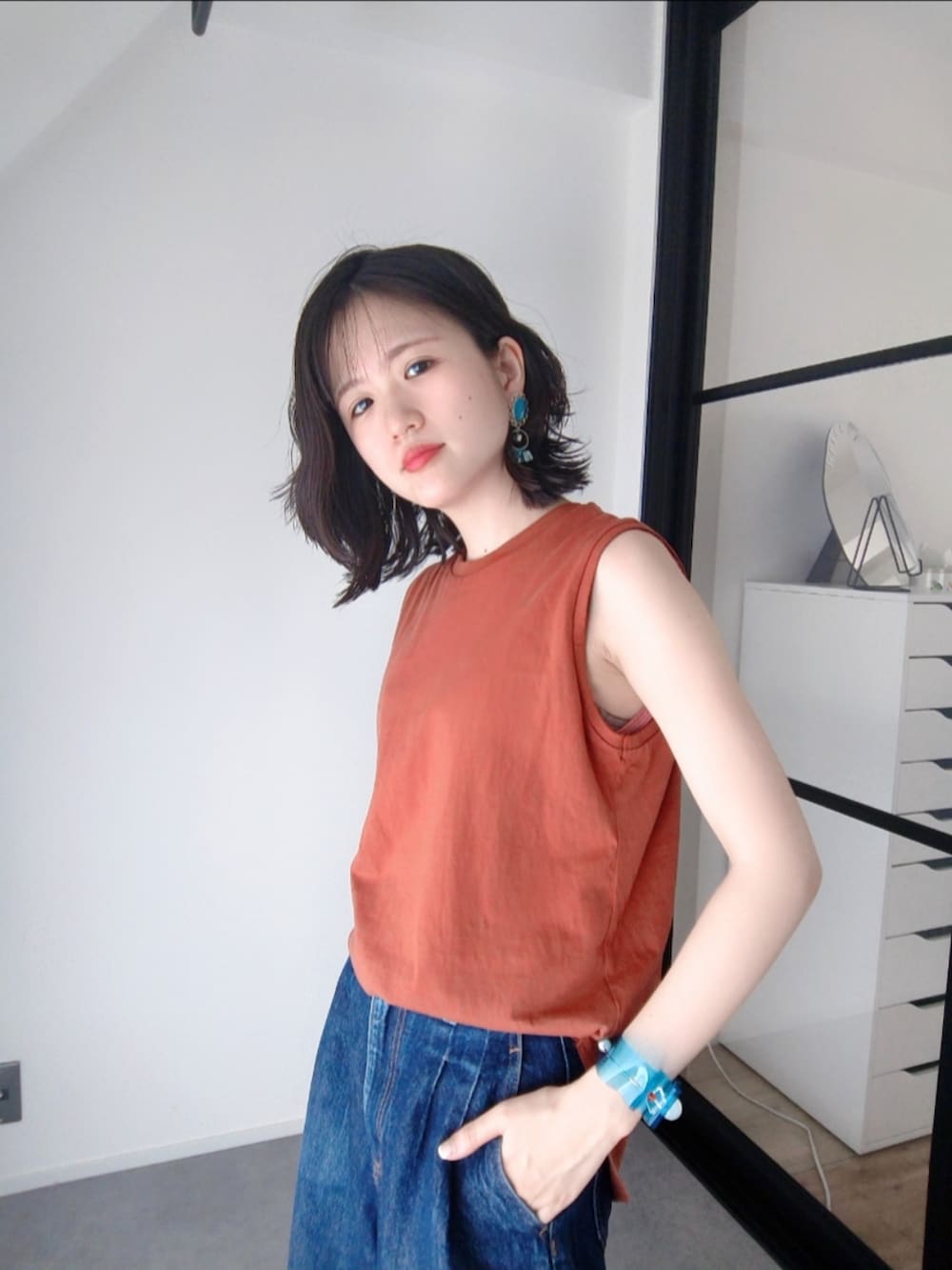 ブルー系のデニムパンツ、ブラック系のサンダル、オレンジ系のタンクトップを着用したレディースの夏コーディネートの2枚目の写真