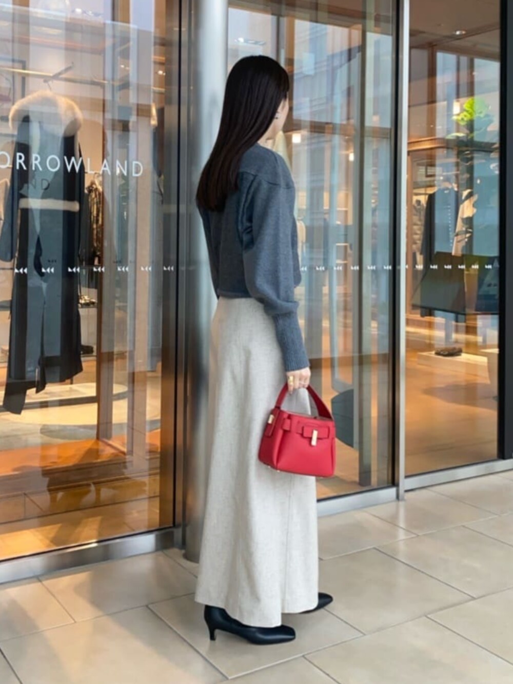 レッド系のハンドバッグ、ブラック系のブーツ、ベージュ系のスカートを着用したレディースの冬コーディネートの2枚目の写真