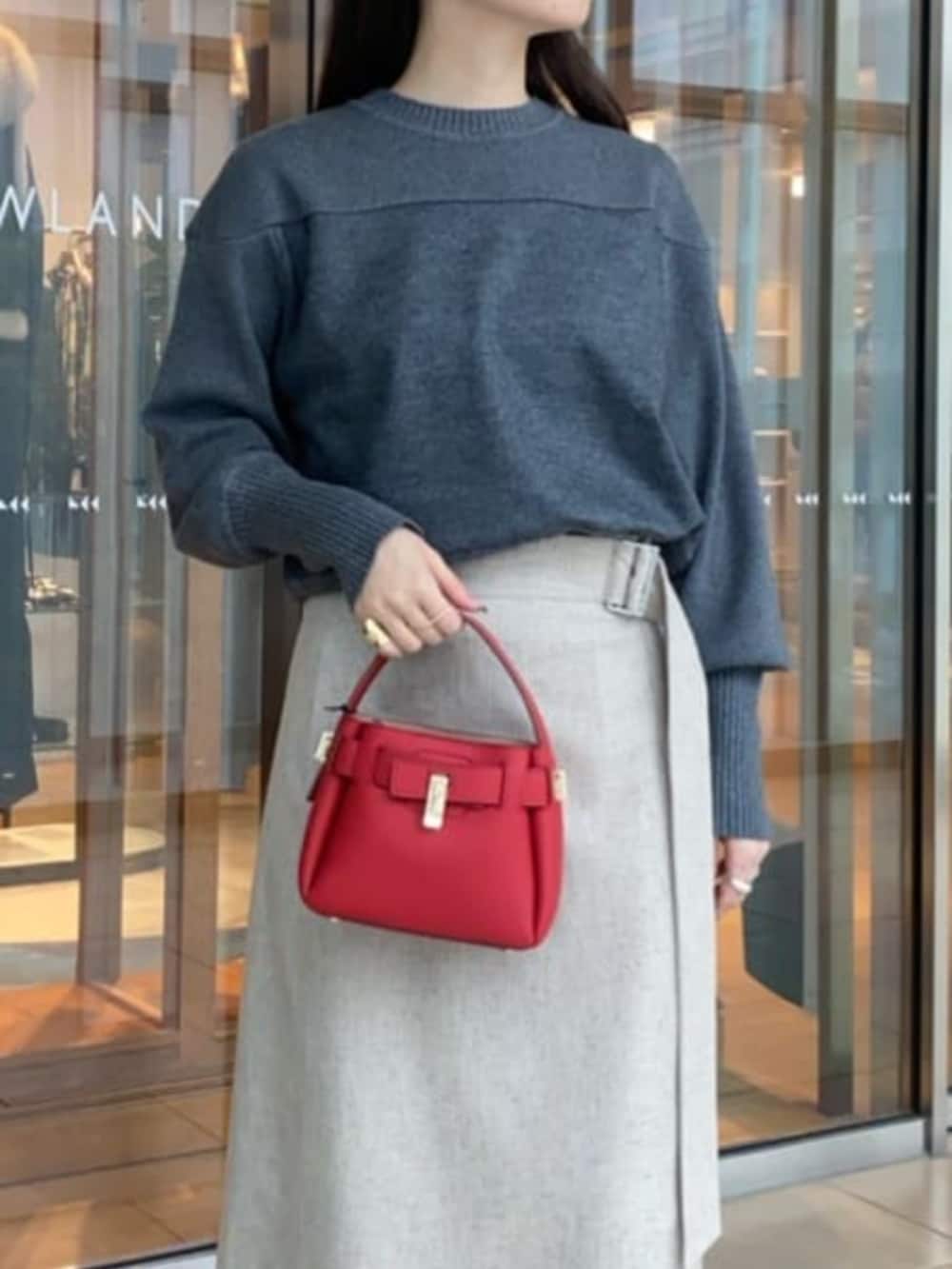 レッド系のハンドバッグ、ブラック系のブーツ、ベージュ系のスカートを着用したレディースの冬コーディネートの3枚目の写真