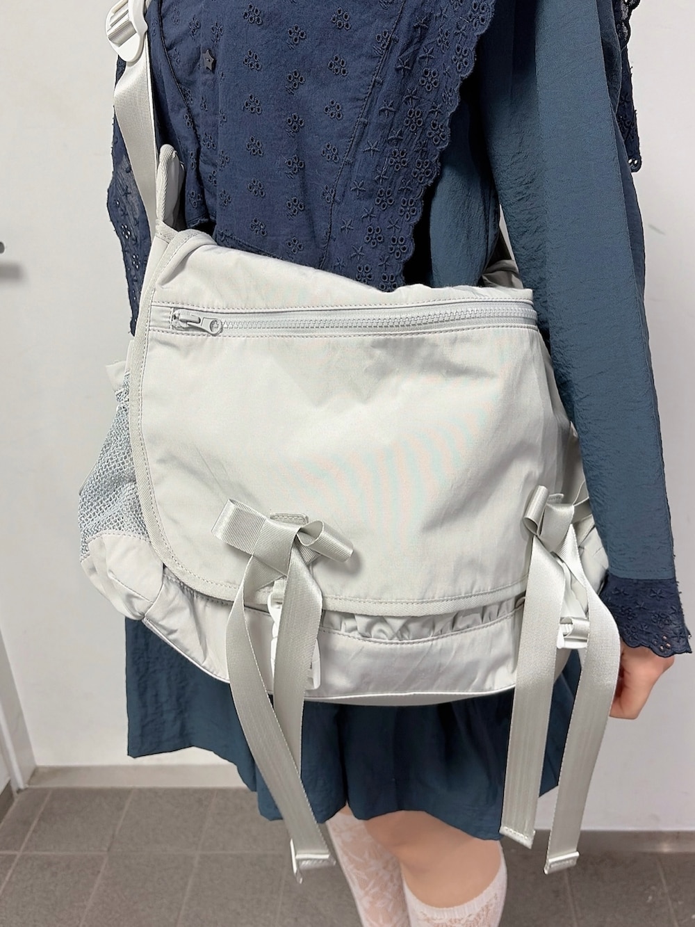 ブルー系のワンピース、ベージュ系のメッセンジャーバッグ、ブラック系のスニーカーを着用したレディースの冬コーディネートの6枚目の写真