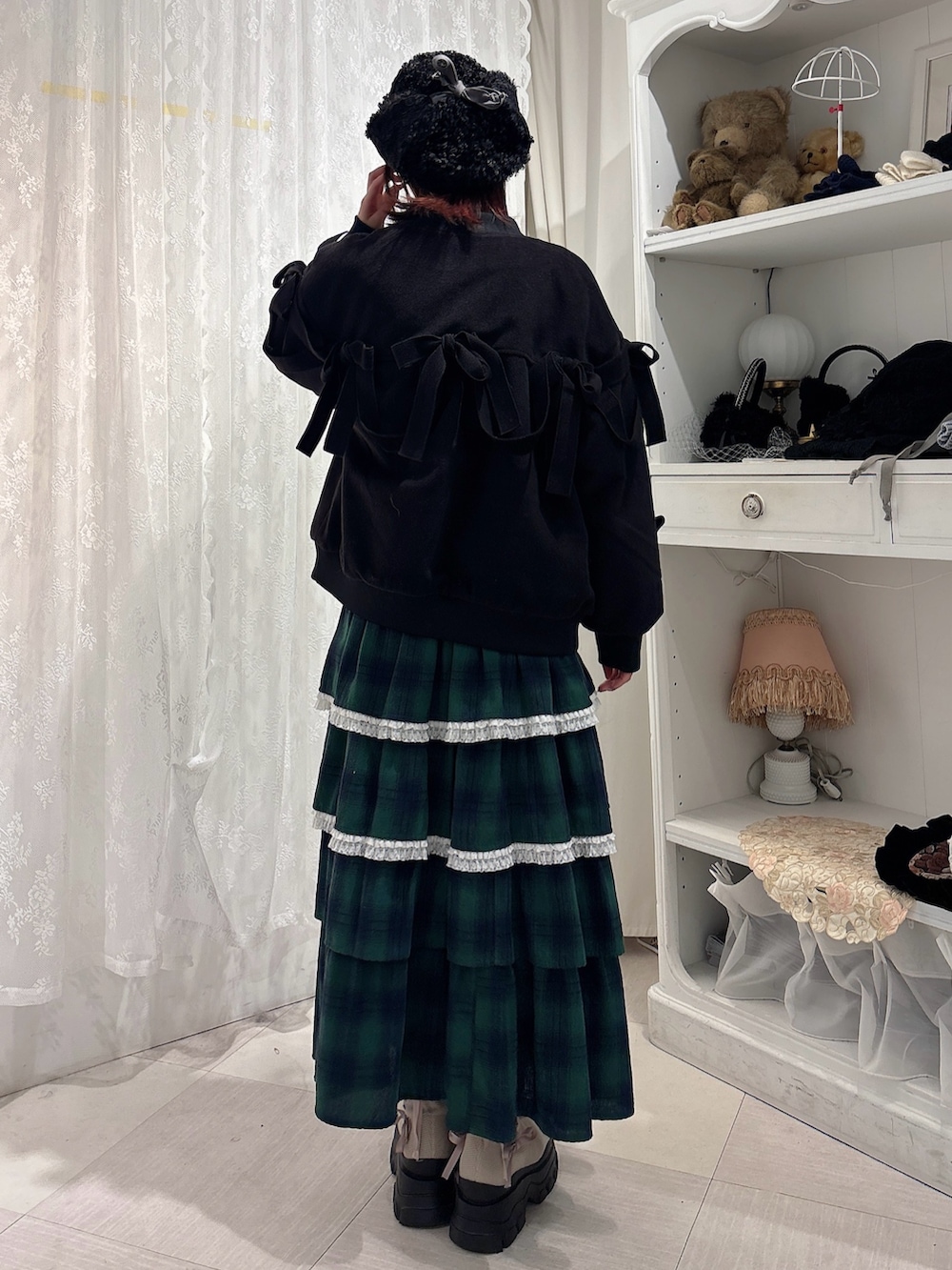 ブラック系のブルゾン、ホワイト系のニット/セーター、グリーン系のスカートを着用したレディースの秋コーディネートの2枚目の写真