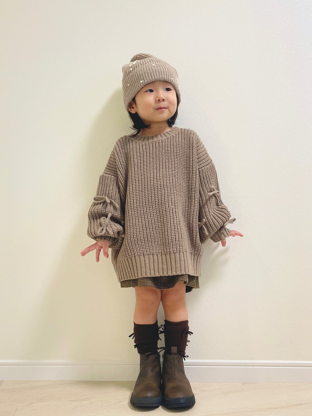 ベージュ系のニット/セーター、ブラウン系のブーツ、ベージュ系のニットキャップ/ビーニーを着用したキッズの秋コーディネートの2枚目の写真