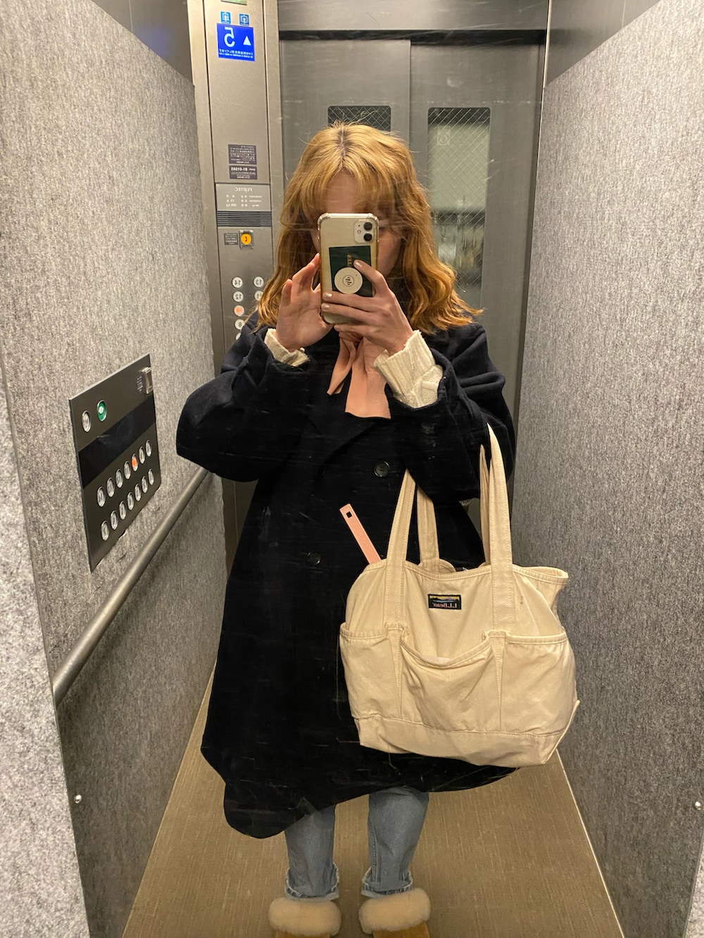 ブラック系のピーコート、ホワイト系のトートバッグ、ブルー系のデニムパンツを着用したレディースの冬コーディネートの2枚目の写真