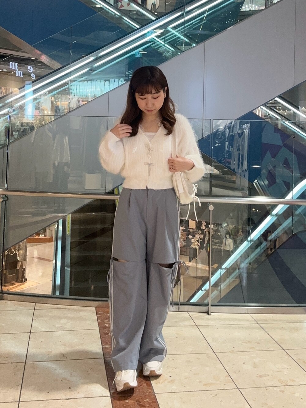 ホワイト系のカーディガン/ボレロ、ホワイト系のショルダーバッグ、ブルー系のスラックスを着用したレディースの秋コーディネートの2枚目の写真