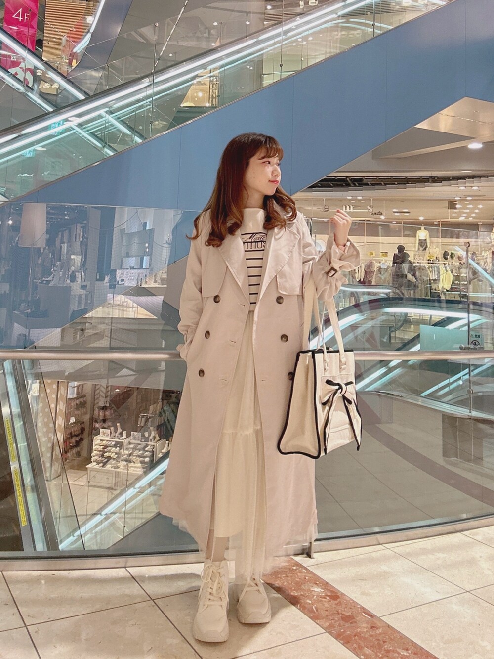 ベージュ系のトレンチコート、ホワイト系のスニーカー、ホワイト系のトートバッグを着用したレディースの冬コーディネートの2枚目の写真