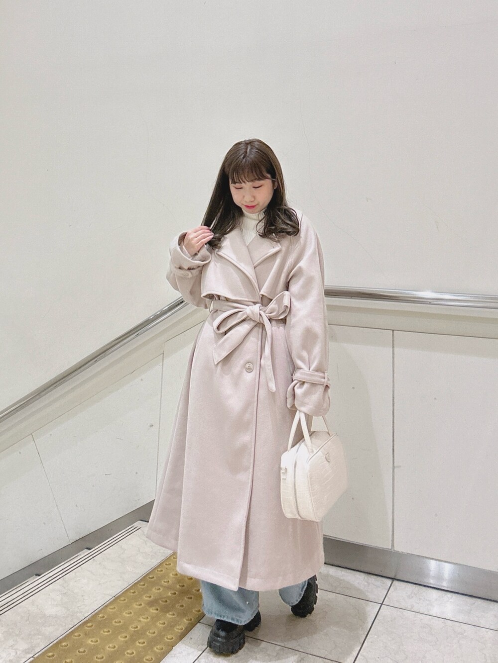 ホワイト系のショルダーバッグ、ホワイト系のニット/セーター、ホワイト系のステンカラーコートを着用したレディースの冬コーディネートの2枚目の写真