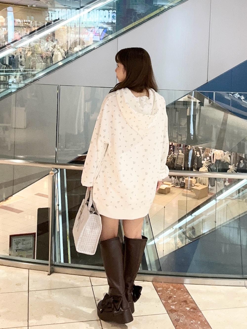 ホワイト系のパーカー、ブルー系のトートバッグ、ブラウン系のブーツを着用したレディースの秋コーディネートの3枚目の写真