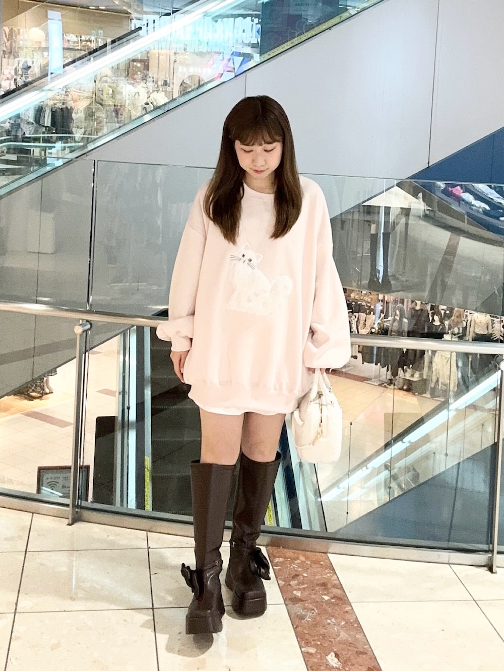 ピンク系のスウェット、ブラウン系のブーツ、ホワイト系のショルダーバッグを着用したレディースの秋コーディネートの2枚目の写真