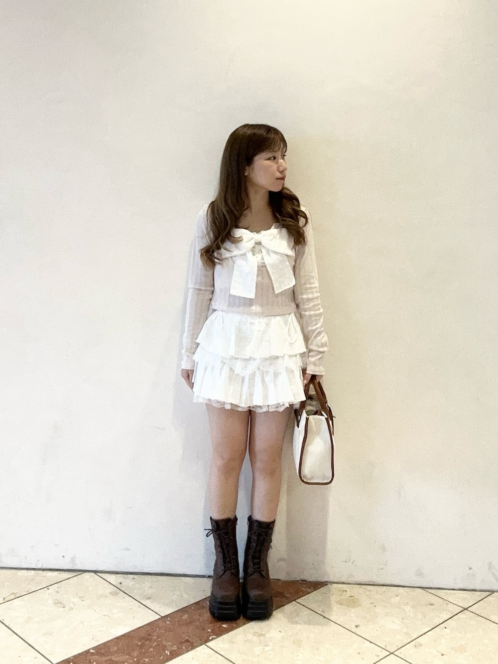 ブラウン系のトートバッグ、ピンク系のTシャツ/カットソー、ホワイト系のスカートを着用したレディースの春コーディネートの2枚目の写真