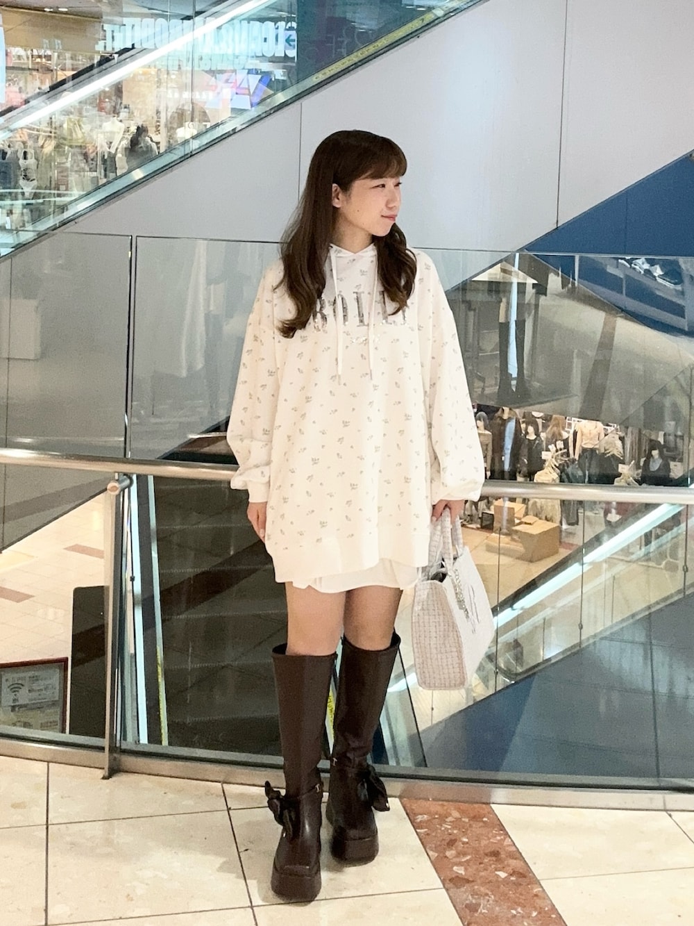 ホワイト系のパーカー、ブルー系のトートバッグ、ブラウン系のブーツを着用したレディースの秋コーディネートの2枚目の写真