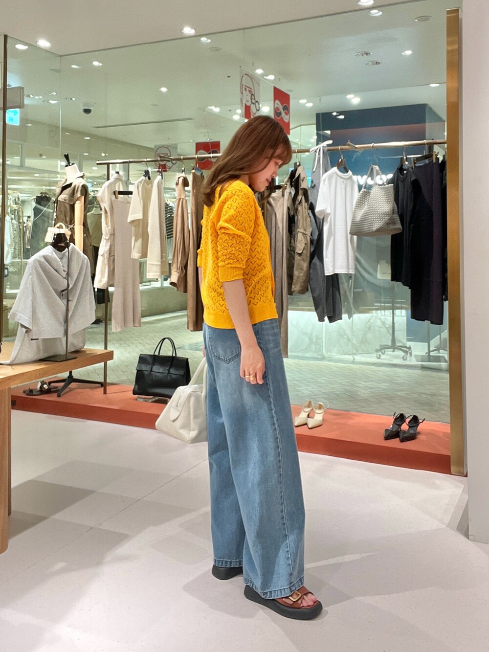 オレンジ系のニット/セーター、ホワイト系のトートバッグ、ブルー系のデニムパンツを着用したレディースの夏コーディネートの2枚目の写真