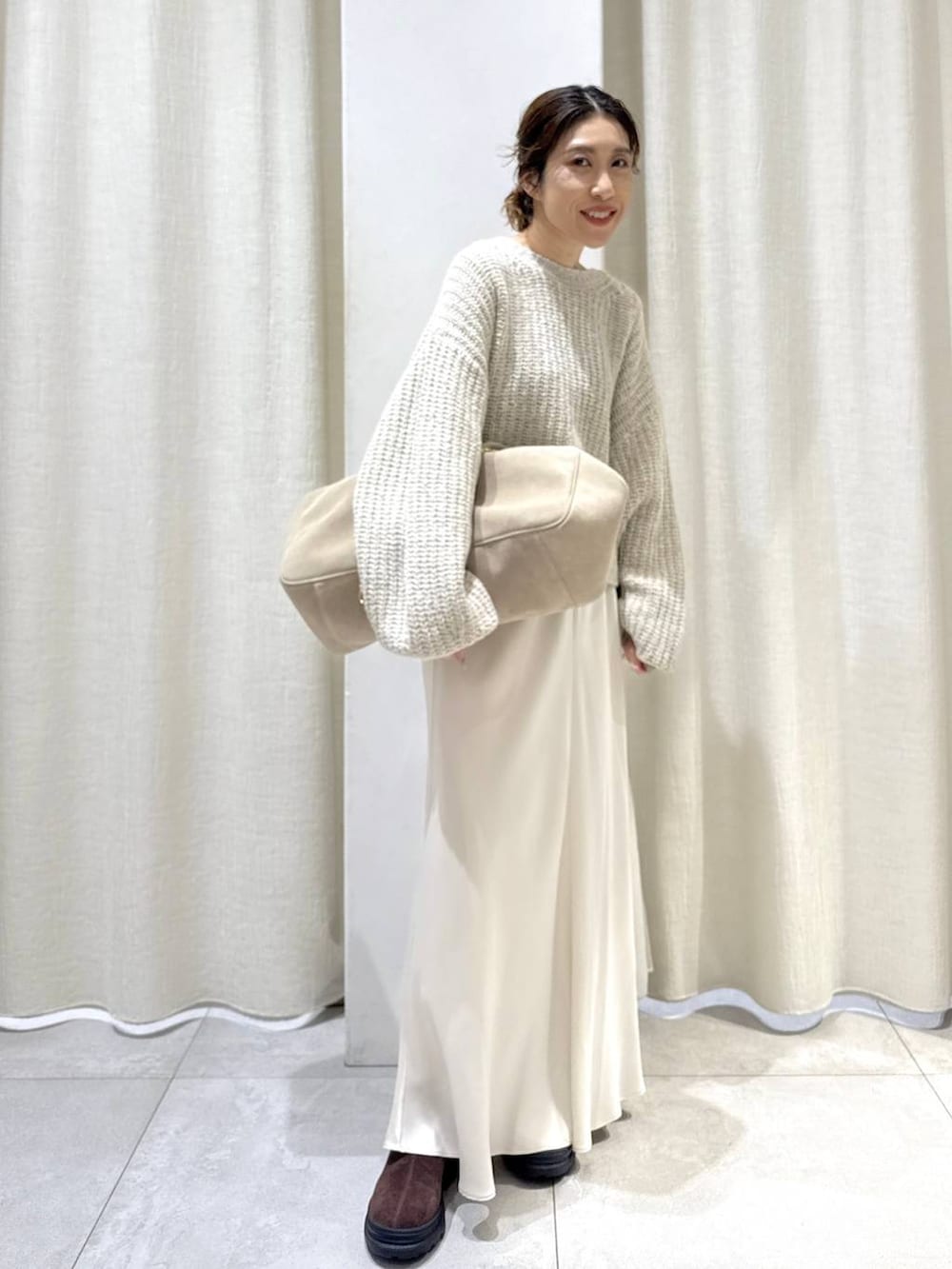 ベージュ系のボストンバッグ、ブラウン系のブーツ、ベージュ系のニット/セーターを着用したレディースの秋コーディネートの2枚目の写真