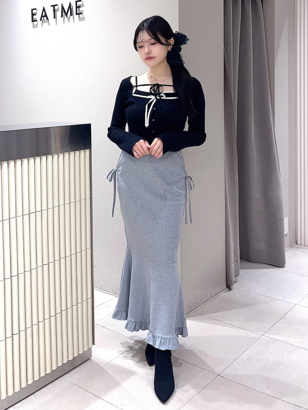 ブラック系のニット/セーター、グレー系のスカート、ブラック系のブーツを着用したレディースの秋コーディネートの2枚目の写真