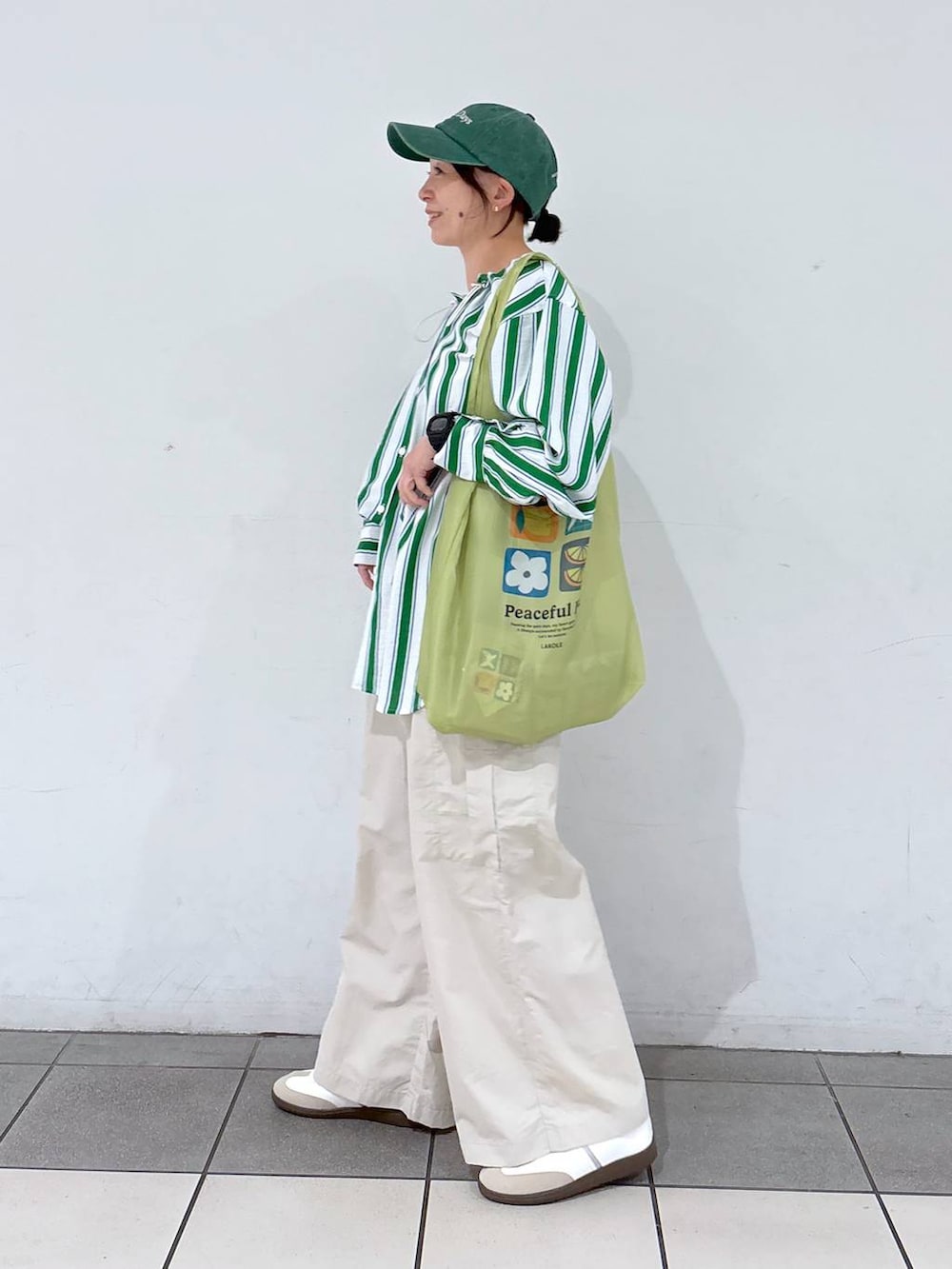 グリーン系のエコバッグ/サブバッグ、ホワイト系のスニーカー、グリーン系のシャツ/ブラウスを着用したレディースの春コーディネートの4枚目の写真