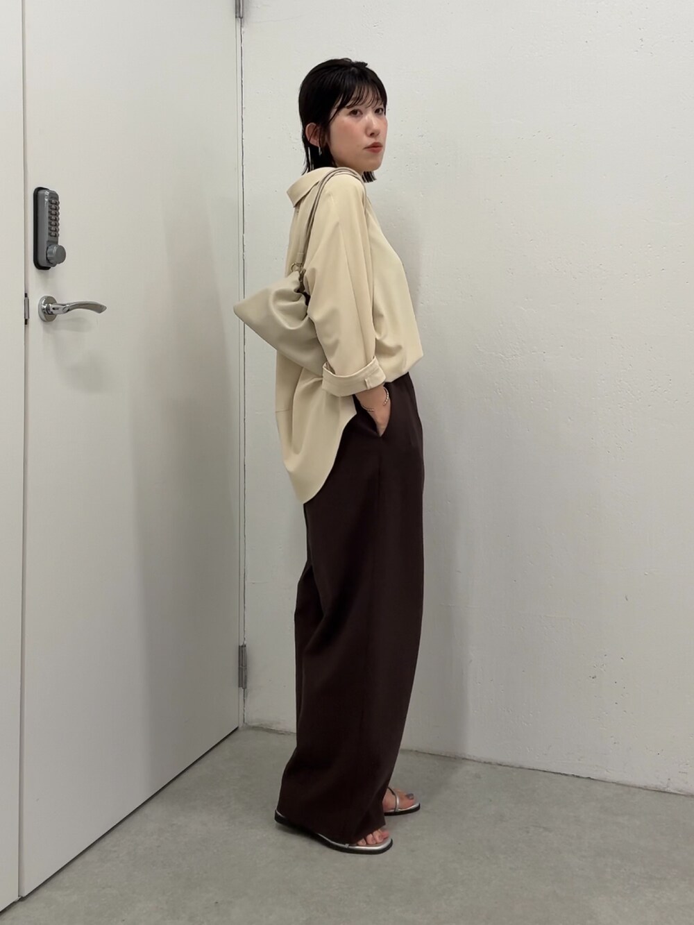 イエロー系のシャツ/ブラウス、ブラウン系のスラックス、ホワイト系のショルダーバッグを着用したレディースの春コーディネートの2枚目の写真