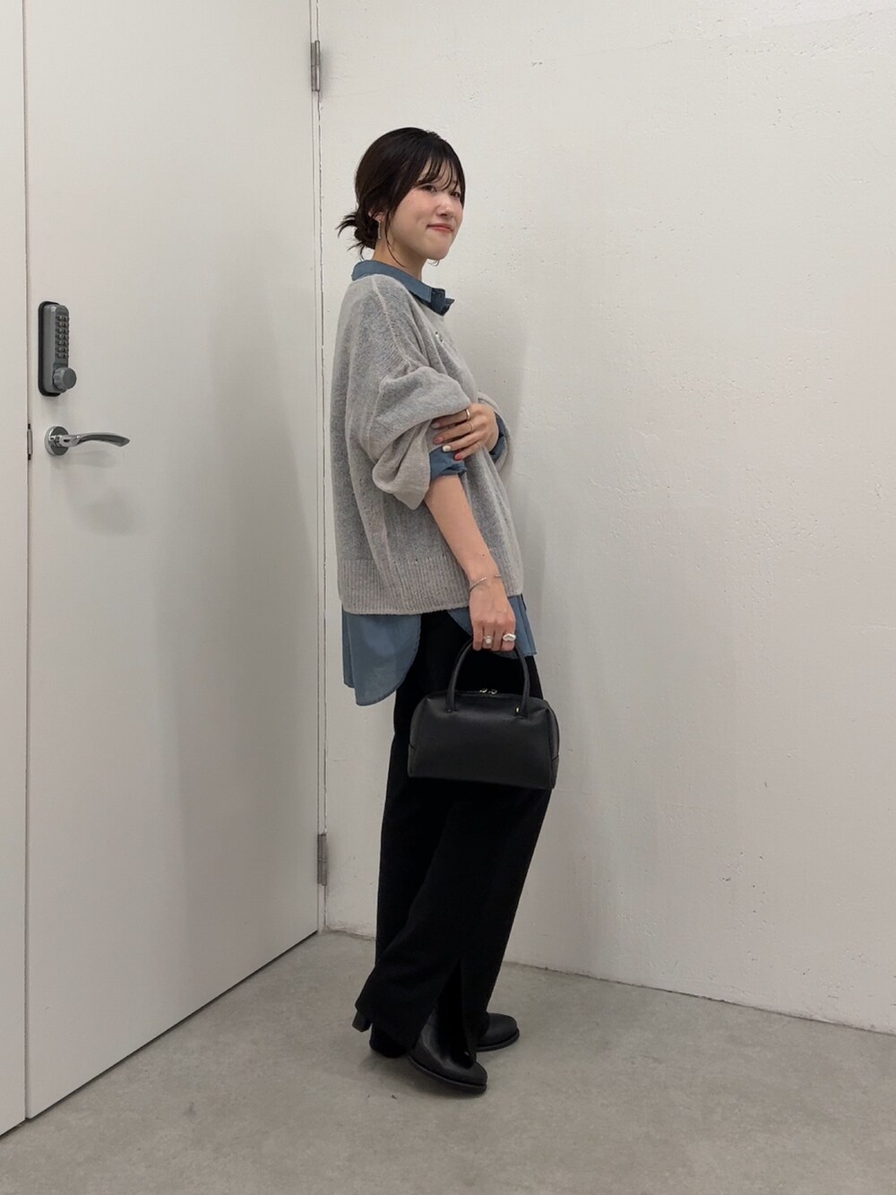 グレー系のニット/セーター、ブルー系のシャツ/ブラウス、ブラック系のボストンバッグを着用したレディースの秋コーディネートの2枚目の写真