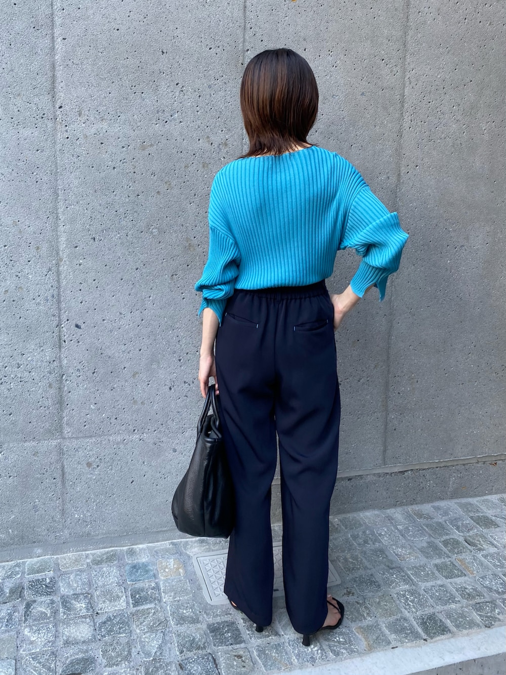 ブラック系のトートバッグ、ブルー系のニット/セーター、ブルー系のスラックスを着用したレディースの夏コーディネートの5枚目の写真