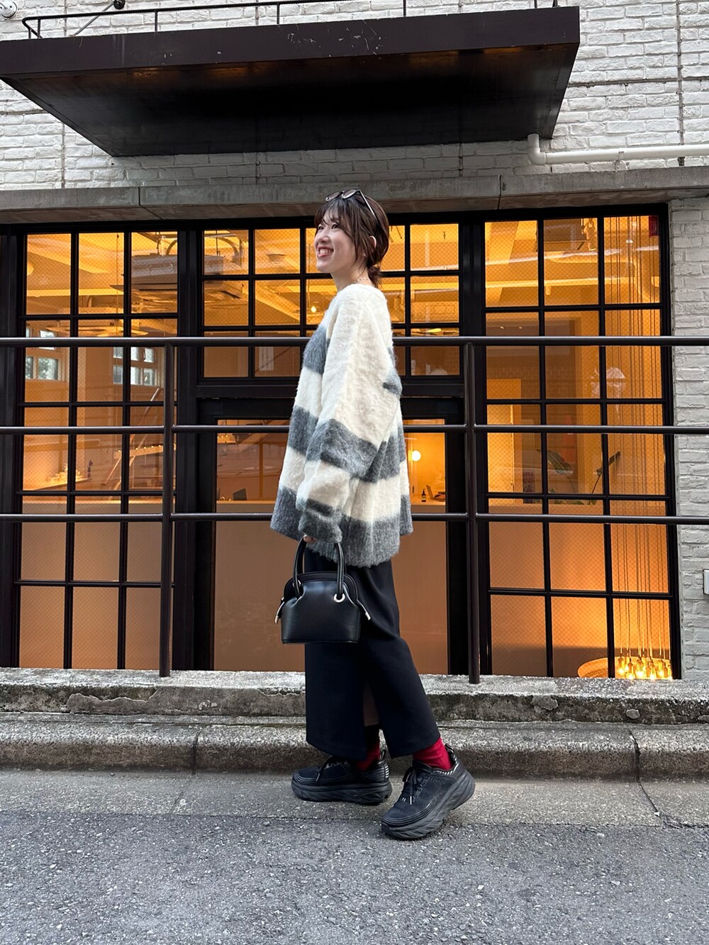 グレー系のニット/セーター、ブラック系のスカート、ブラック系のバッグを着用したレディースの秋コーディネートの2枚目の写真