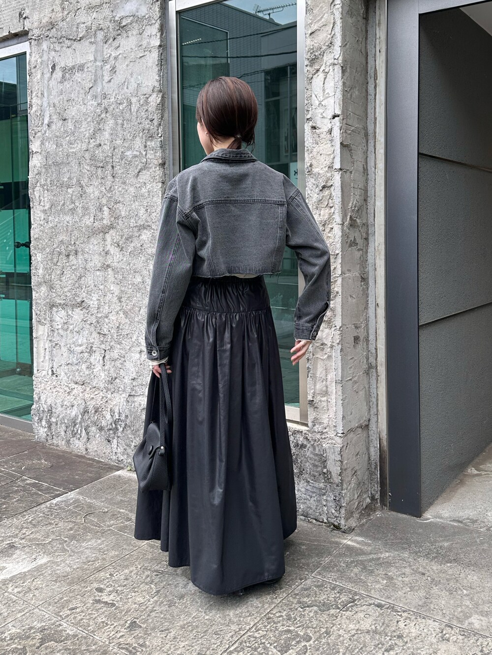 ブラック系のデニムジャケット、ホワイト系のニット/セーター、ブラック系のスカートを着用したレディースの夏コーディネートの2枚目の写真