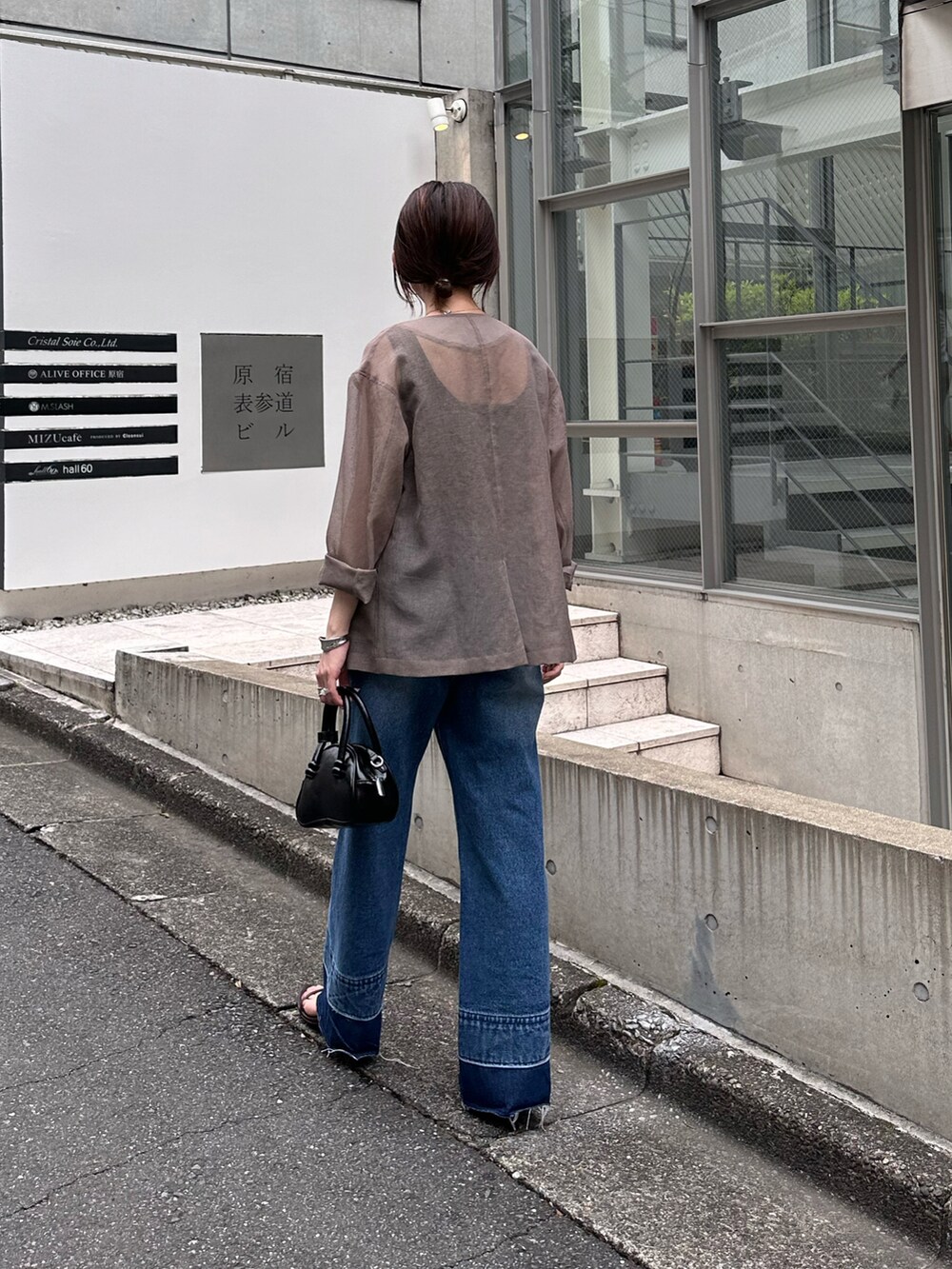 ブラック系のバッグ、ブラウン系のノーカラージャケット、ブルー系のデニムパンツを着用したレディースの夏コーディネートの3枚目の写真