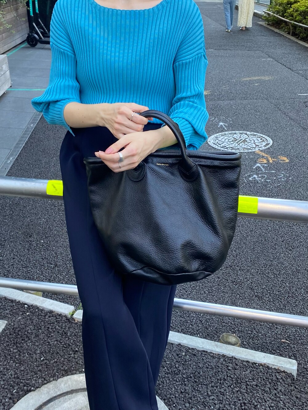 ブラック系のトートバッグ、ブルー系のニット/セーター、ブルー系のスラックスを着用したレディースの夏コーディネートの2枚目の写真