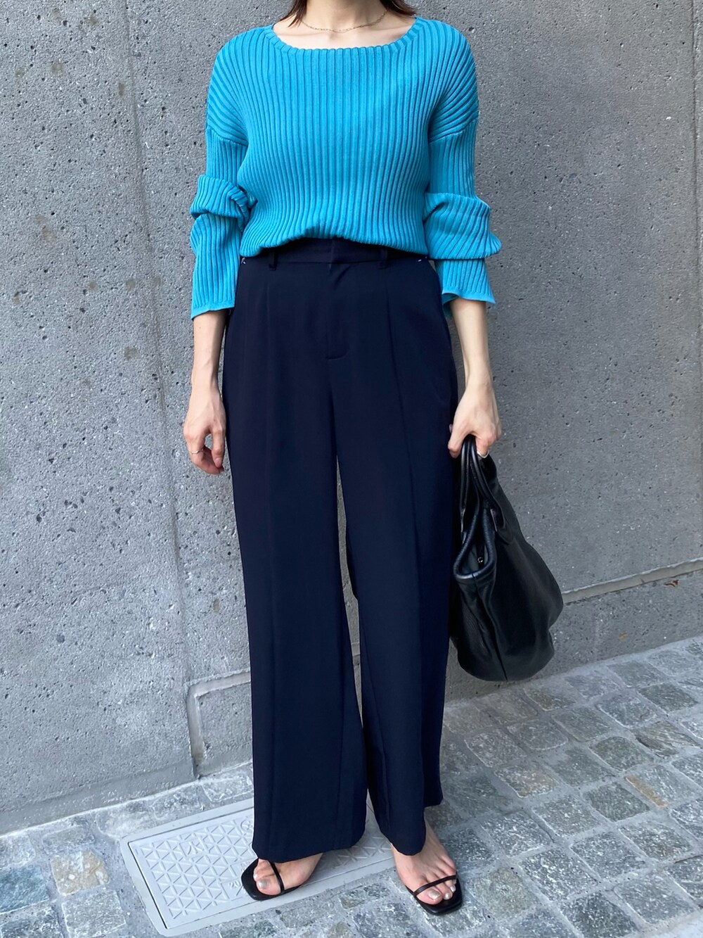 ブラック系のトートバッグ、ブルー系のニット/セーター、ブルー系のスラックスを着用したレディースの夏コーディネートの4枚目の写真