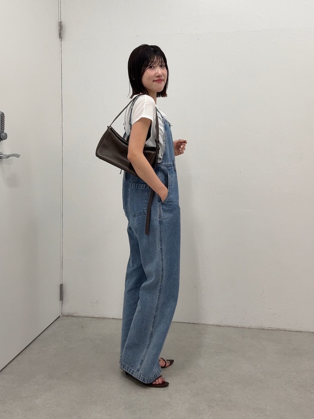 ブルー系のサロペット/オーバーオール、ホワイト系のTシャツ/カットソー、ブラウン系のショルダーバッグを着用したレディースの春コーディネートの2枚目の写真