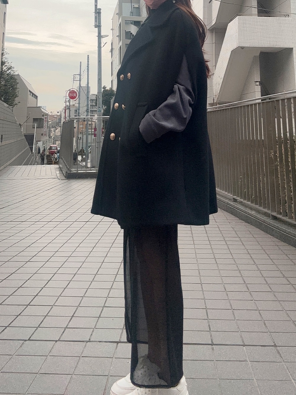 ブラック系のスカート、ホワイト系のスニーカー、ブラック系のポンチョを着用したレディースの冬コーディネートの2枚目の写真