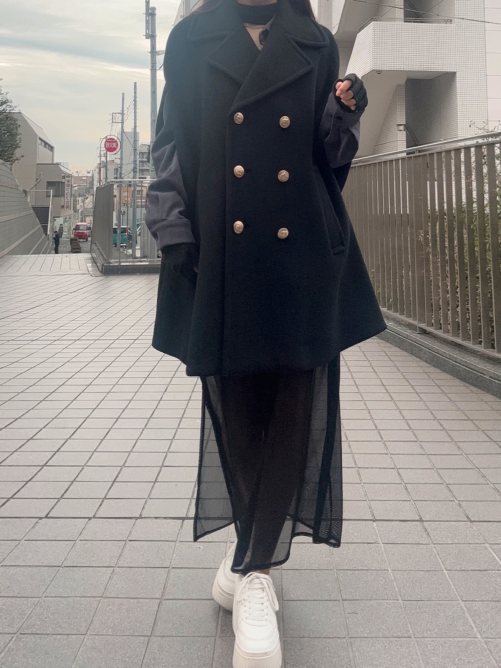 ブラック系のスカート、ホワイト系のスニーカー、ブラック系のポンチョを着用したレディースの冬コーディネートの4枚目の写真