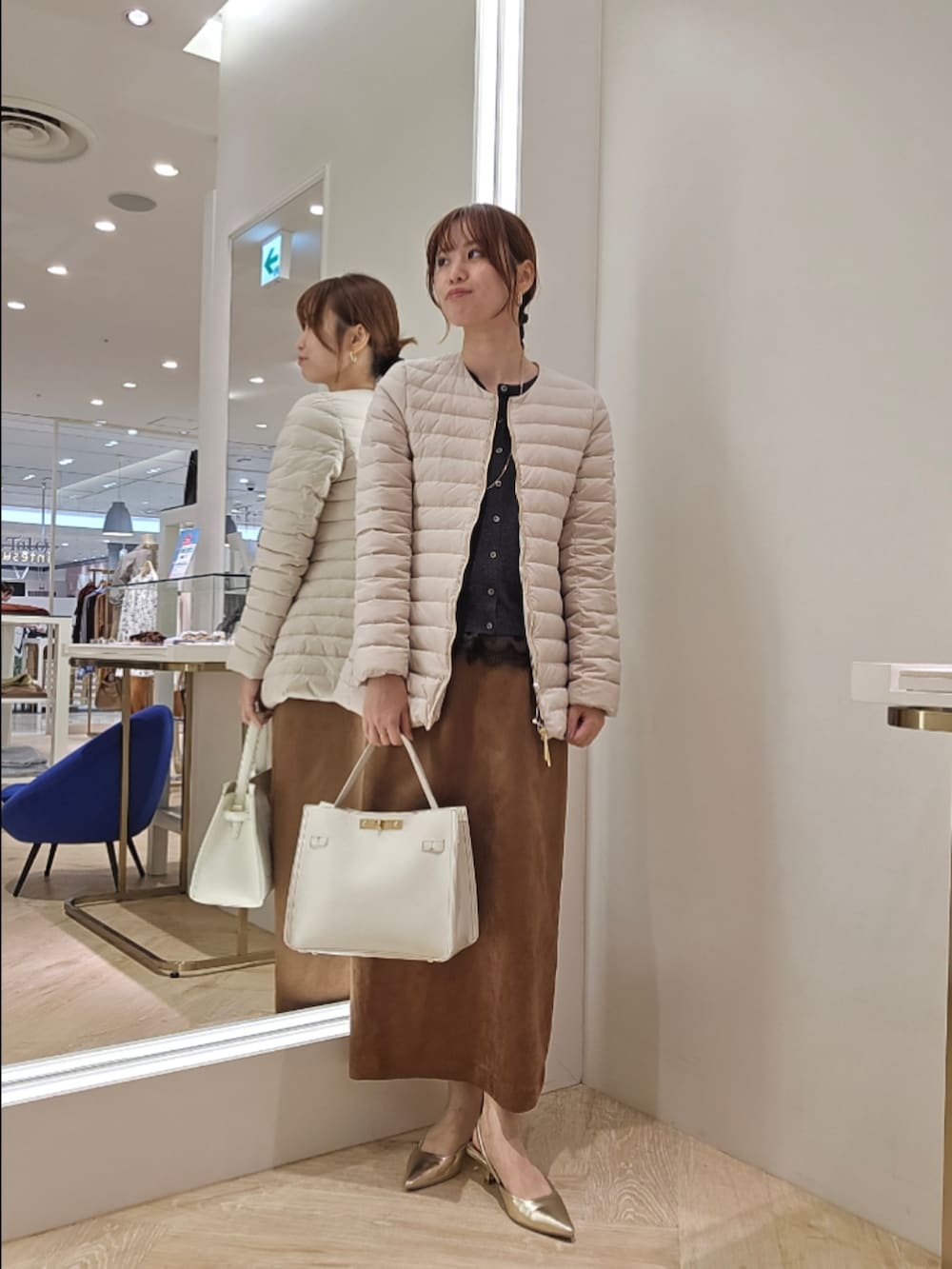 イエロー系のスカート、ベージュ系のダウンジャケット/コート、グレー系のカーディガン/ボレロを着用したレディースの秋コーディネートの2枚目の写真