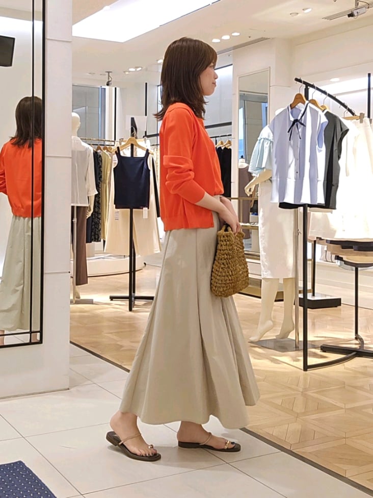 オレンジ系のニット/セーター、オレンジ系のカーディガン/ボレロ、ベージュ系のスカートを着用したレディースの夏コーディネートの3枚目の写真