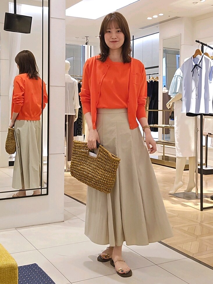 オレンジ系のニット/セーター、オレンジ系のカーディガン/ボレロ、ベージュ系のスカートを着用したレディースの夏コーディネートの2枚目の写真