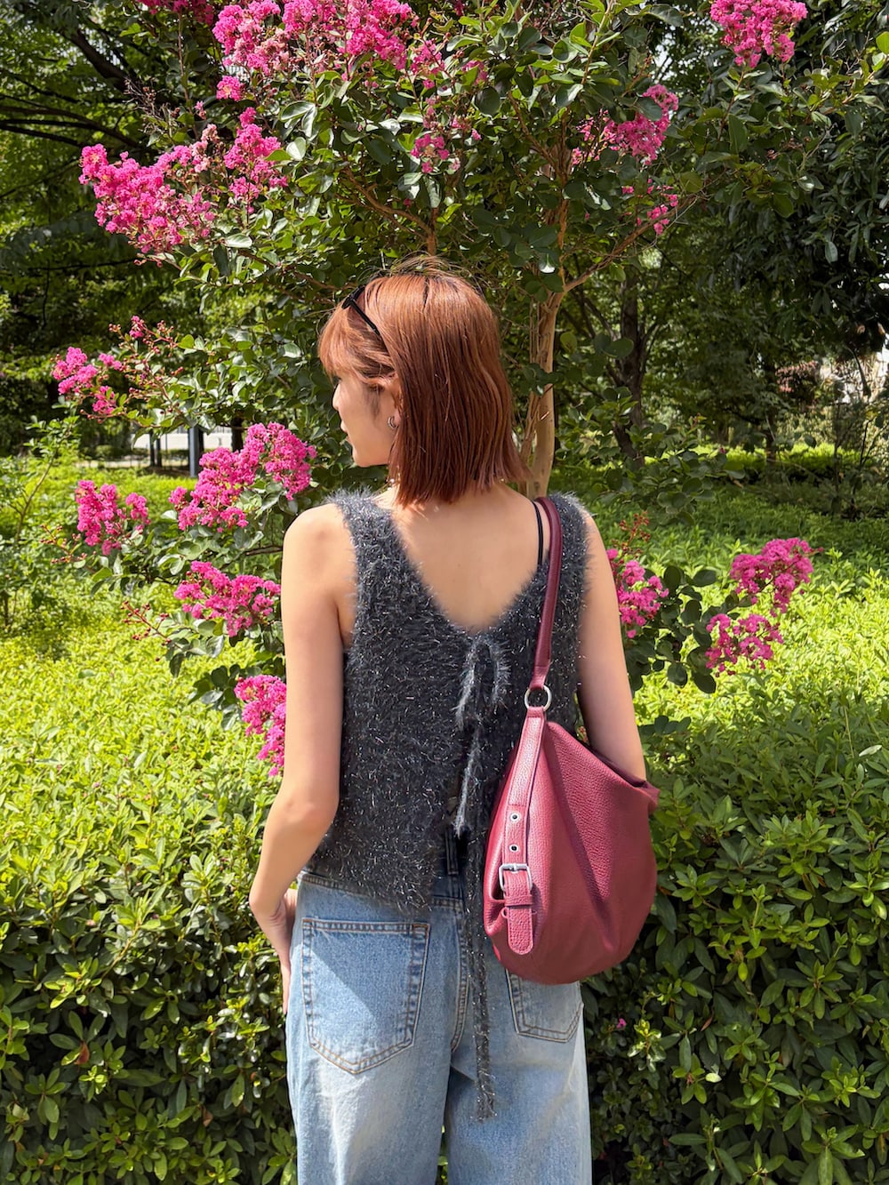 グレー系のベスト、ブルー系のデニムパンツ、レッド系のショルダーバッグを着用したレディースの夏コーディネートの3枚目の写真