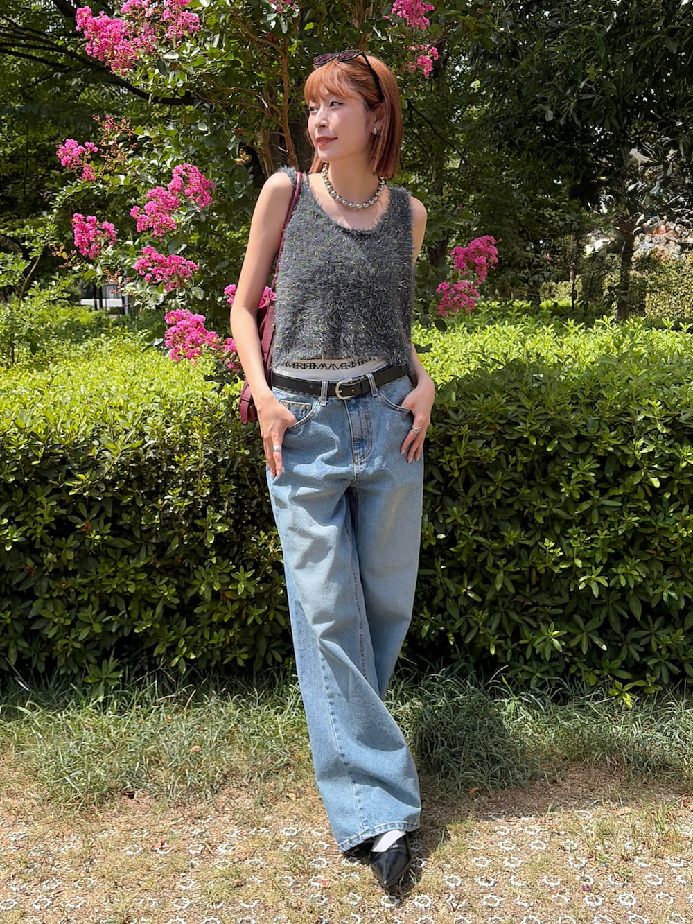 グレー系のベスト、ブルー系のデニムパンツ、レッド系のショルダーバッグを着用したレディースの夏コーディネートの2枚目の写真