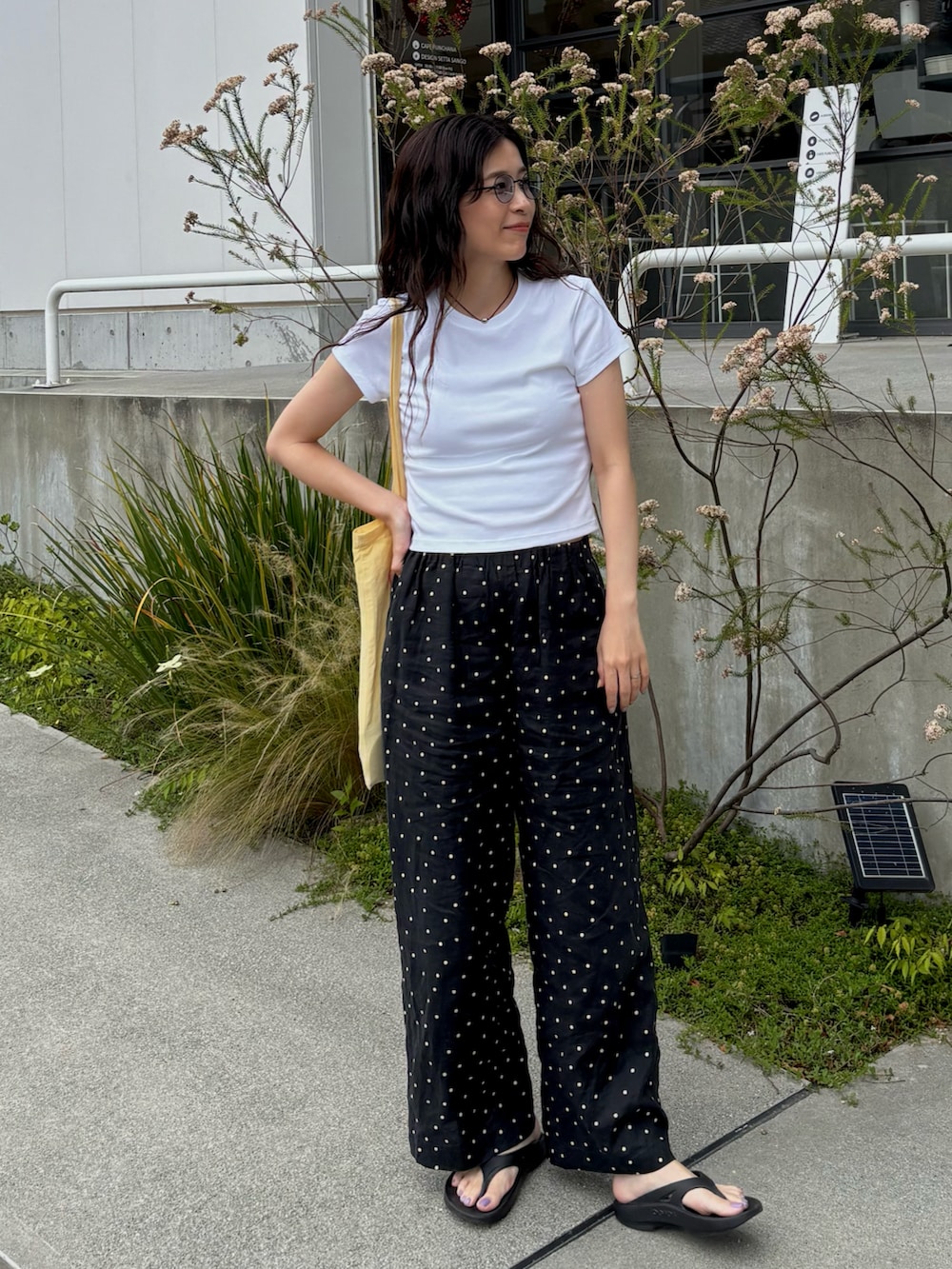 イエロー系のトートバッグ、ブラック系のサンダル、ホワイト系のTシャツ/カットソーを着用したレディースの夏コーディネートの2枚目の写真