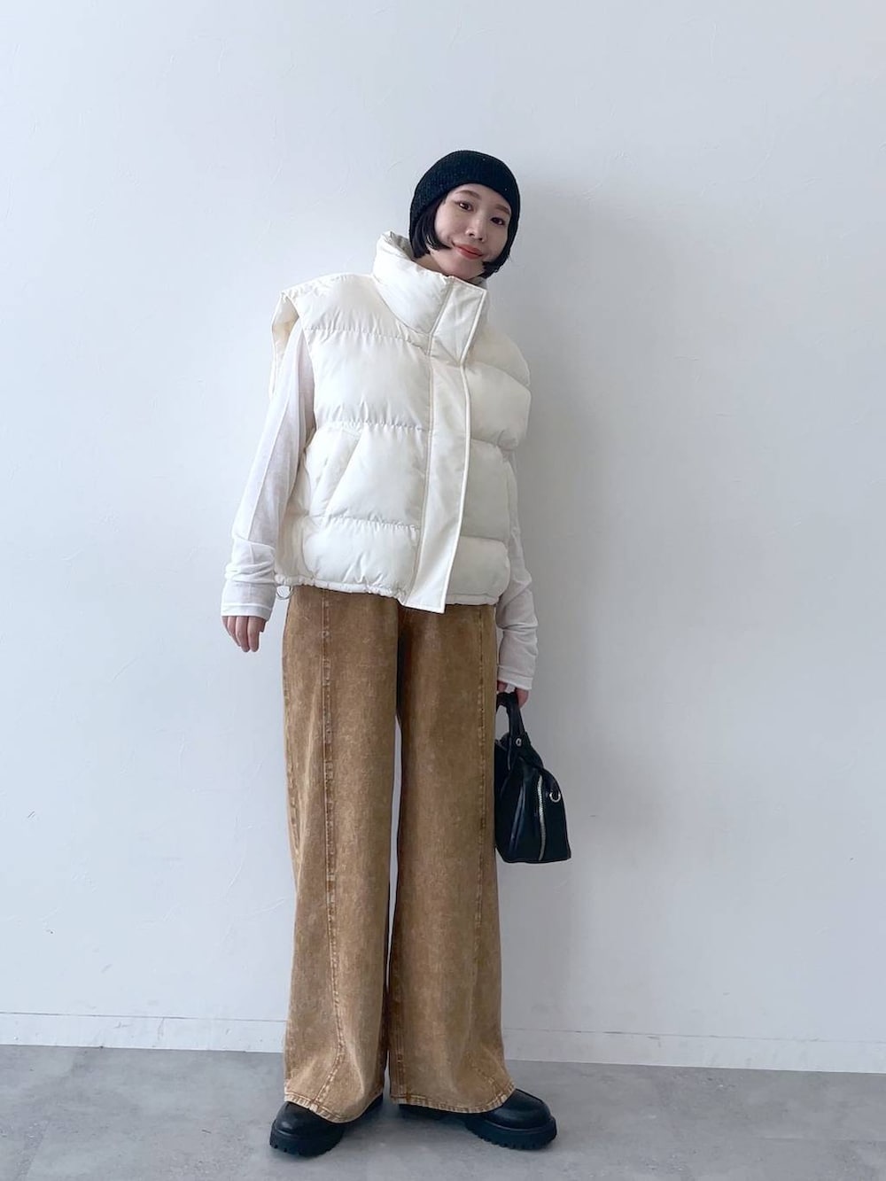 ホワイト系のダウンベスト、ブラウン系のデニムパンツ、ブラック系のニットキャップ/ビーニーを着用したレディースの秋コーディネートの2枚目の写真