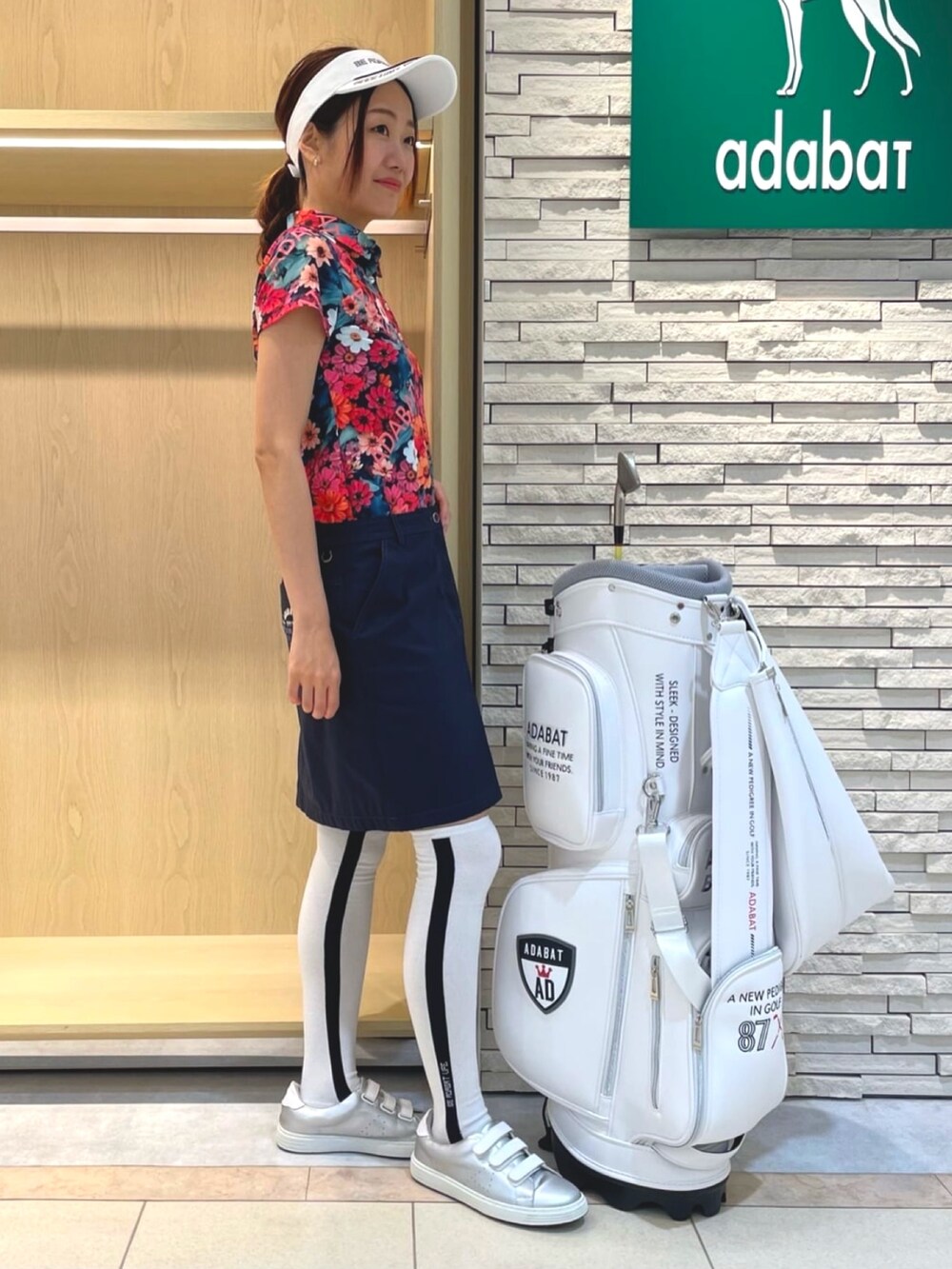 ブルー系のスカート、ピンク系のポロシャツ、ホワイト系のサンバイザーを着用したレディースの夏コーディネートの2枚目の写真