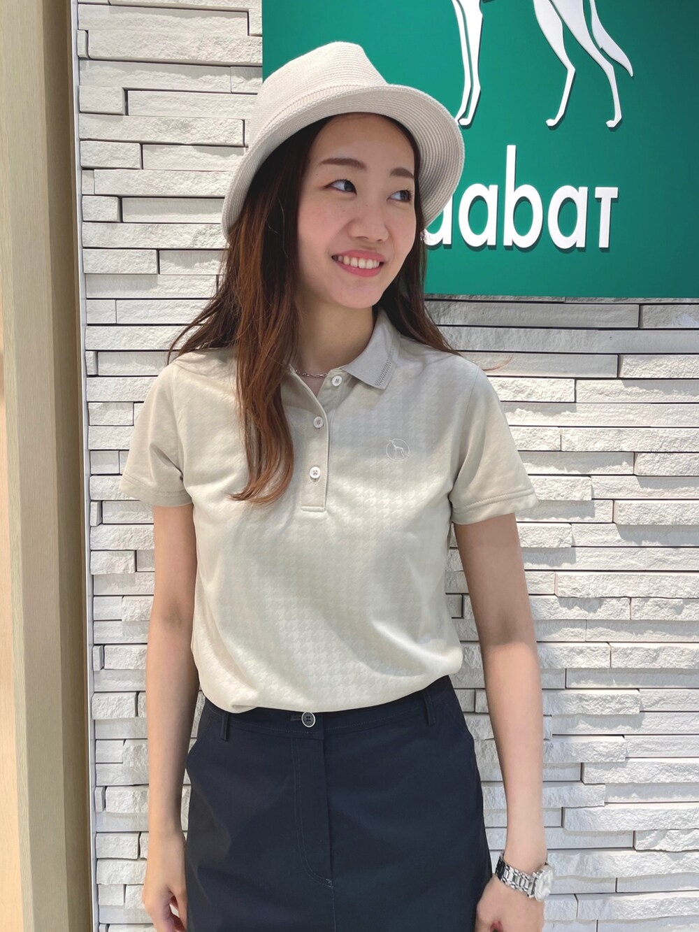 ブラック系のスカート、ベージュ系のポロシャツ、ベージュ系のハットを着用したレディースの夏コーディネートの5枚目の写真